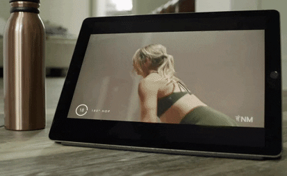 A tablet on a table playing a follow along exercise video.