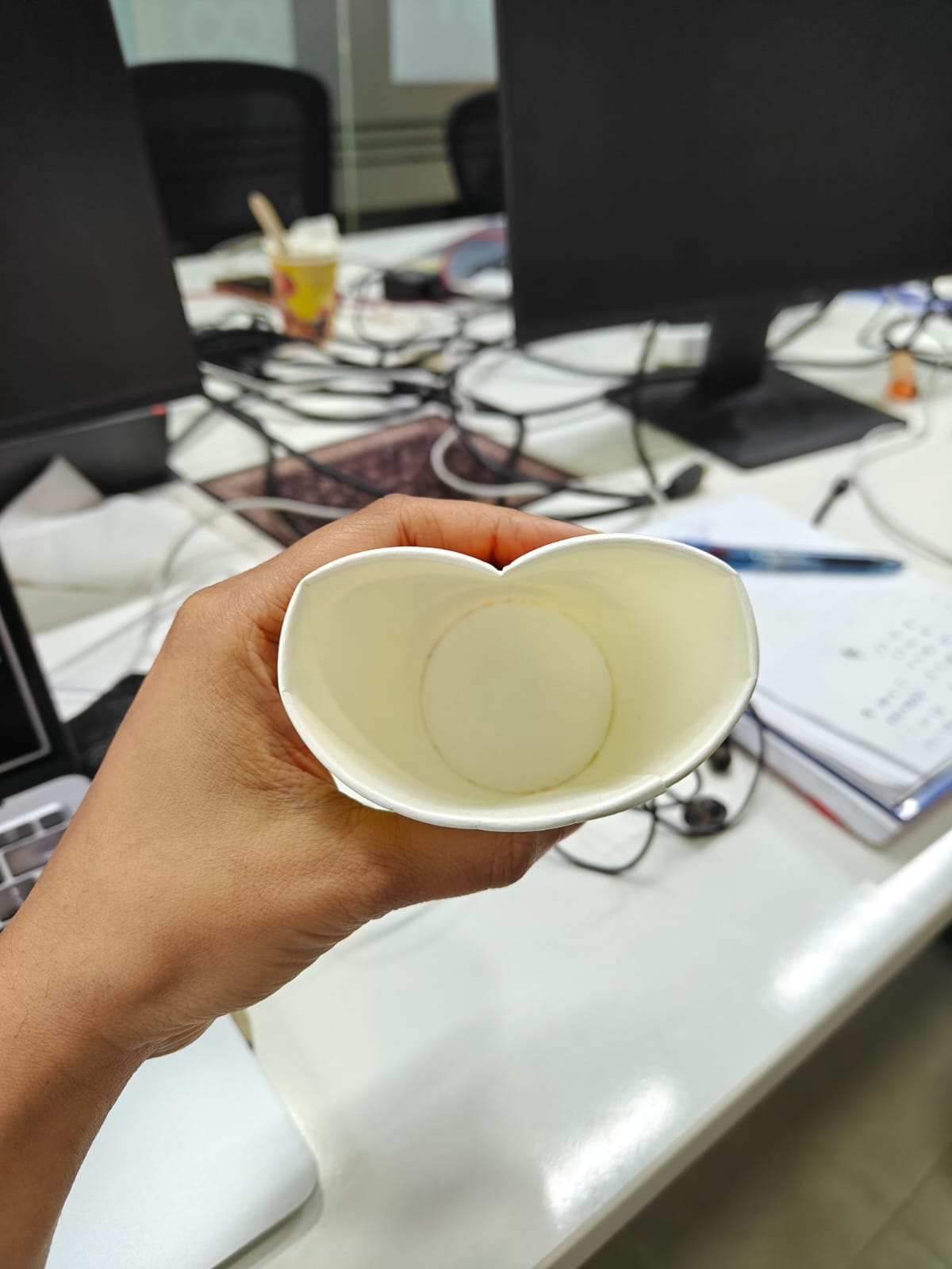 A squashed paper cup held in a hand, then the same cup with a wide grinning mouth and eyes drawn over it.