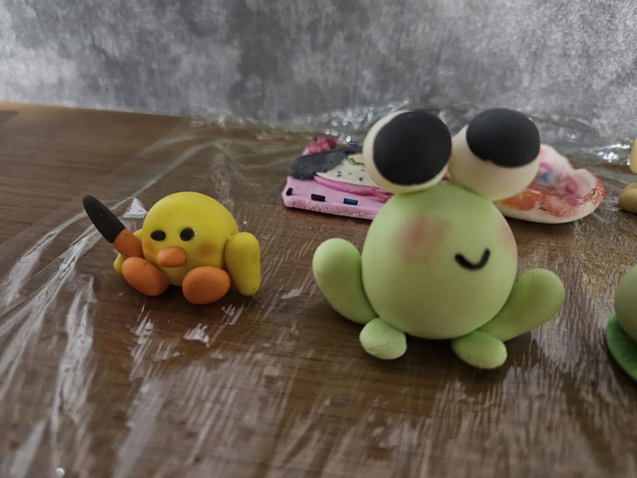 Two clay figures on a table, a yellow duck holding a knife and a green frog with large eyes.
