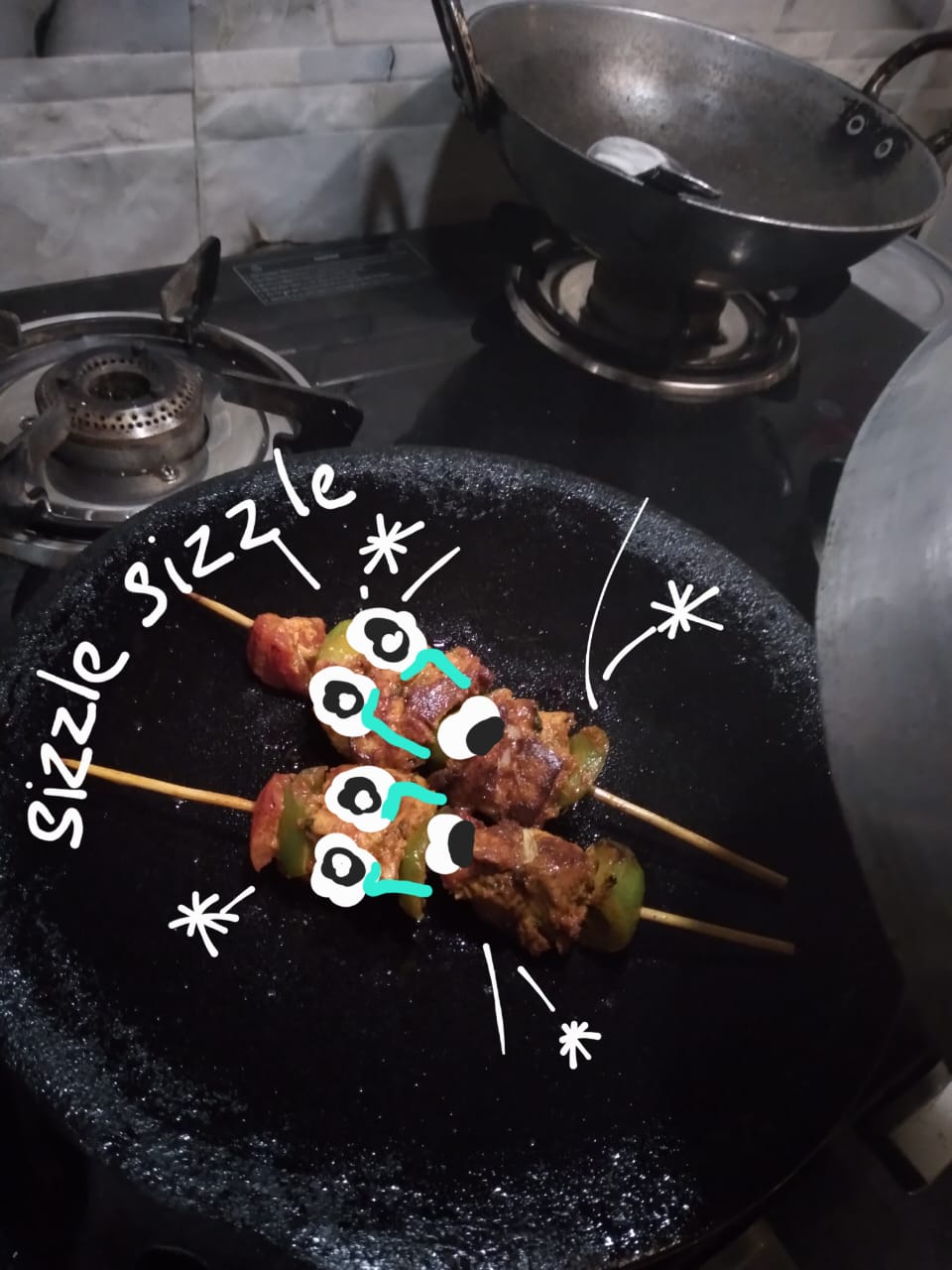 Kebab skewers on a hot pan with eyes drawn on them and the word sizzle lettered beside.
